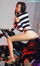 A woman sitting on top of a motorcycle wearing a striped shirt.