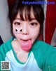 A woman sticking out her tongue with a cat face painted on her face.