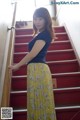 A woman standing on a set of stairs in a blue top and yellow skirt.