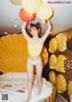 A woman in a yellow bikini holding a bunch of balloons.