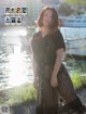 A woman in a sheer black dress posing by the water.