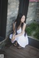 A woman in a white dress sitting on a wooden floor.