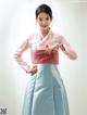 A woman in a pink and blue hanbok poses for a picture.