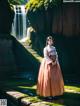 A woman in a long dress standing in front of a waterfall.