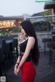 A woman in a black top and red skirt standing on a wooden deck.