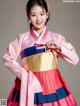 A woman in a pink and blue hanbok poses for a picture.