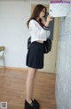 A woman in a school uniform standing in front of lockers.