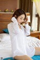 A woman in a white shirt sitting on a bed.