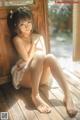 A naked woman sitting on a wooden floor next to a window.