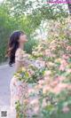 A woman in a floral dress standing in front of a tree.