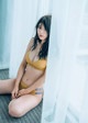 A woman in a yellow bikini sitting on a bed.