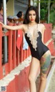A woman in a black bathing suit leaning against a red fence.